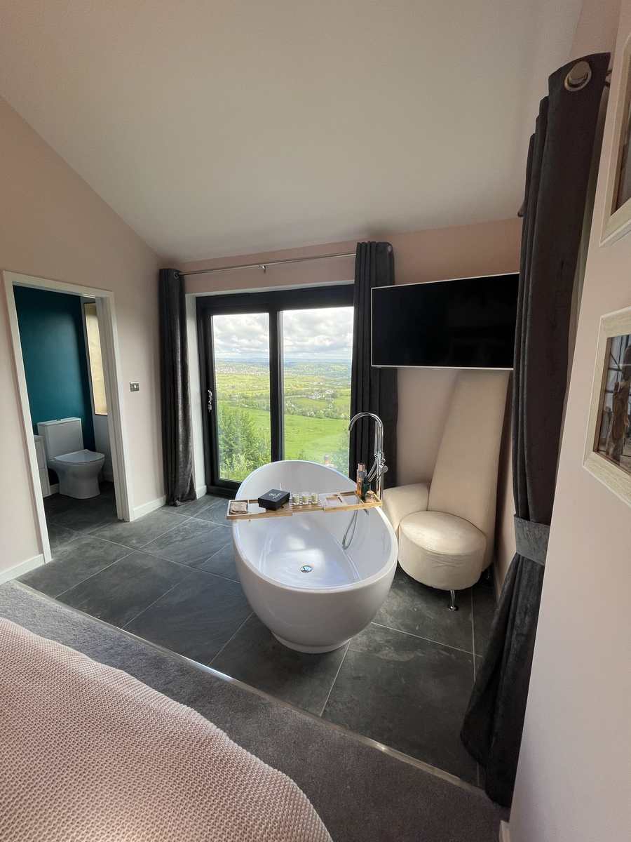 Loft bathroom with a freestanding bath beside glazed doors opening onto open countryside