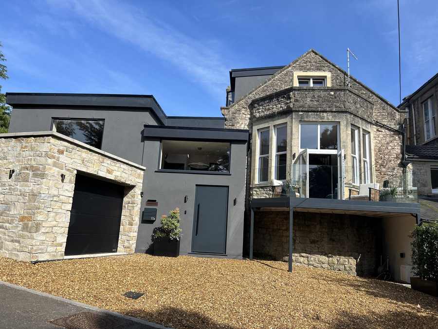 Stone house with a contemporary grey loft conversion above the garage, seen from the driveway