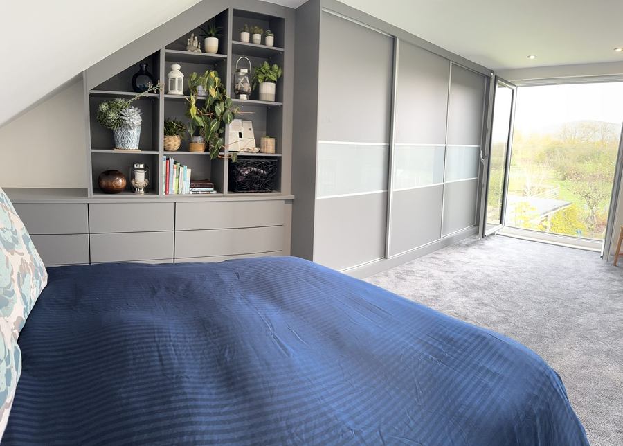 Loft bedroom with fitted wardrobes, built-in shelving and full-height glazed doors onto a rural view